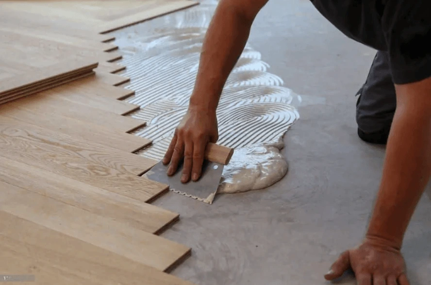 Installer setting engineered hardwood planks into troweled adhesive